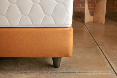 Close up of padded bed base upholstered in custom fabric and with round dark brown wood legs
