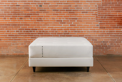 Padded bed base upholstered in organic cotton canvas with black square legs and a natural mattress on top