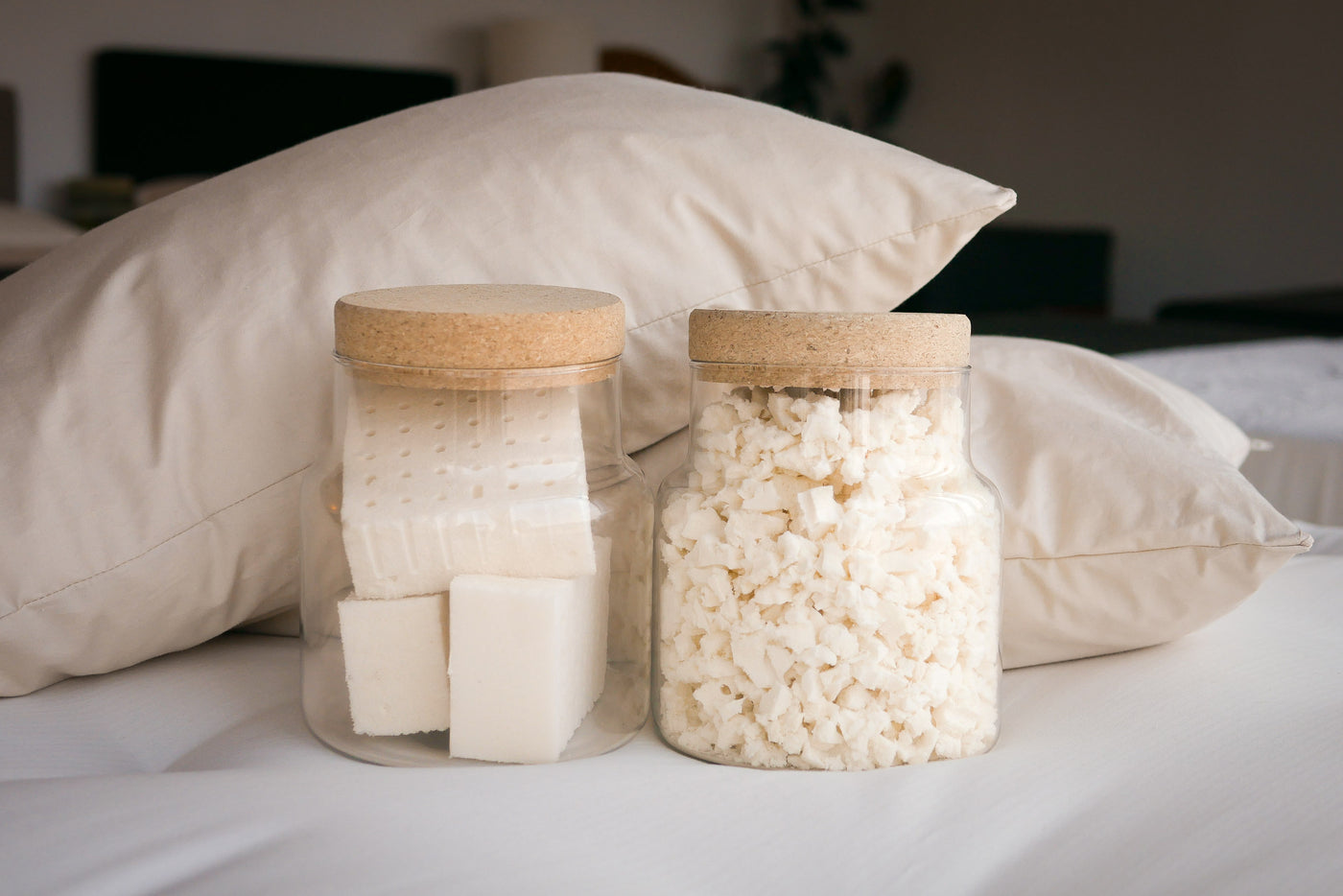 Jars of natural talalay latex and shredded natural talalay latex with two shredded natural latex pillows in the background