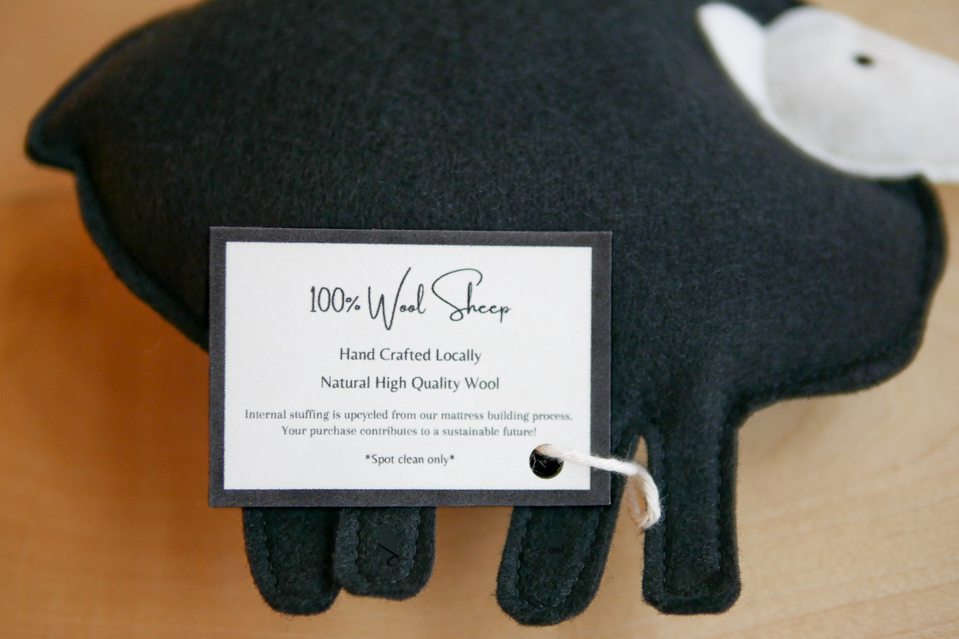 Tag on wool sheep toy that says 100% wool sheep, hand crafted locally, natural high quality wool, internal stuffing is upcycled from our mattress building process. Your purchase contributes to a sustainable future! Spot clean only.