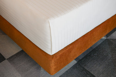 Natural stripe sateen flat sheet tucked into mattress on a custom padded base