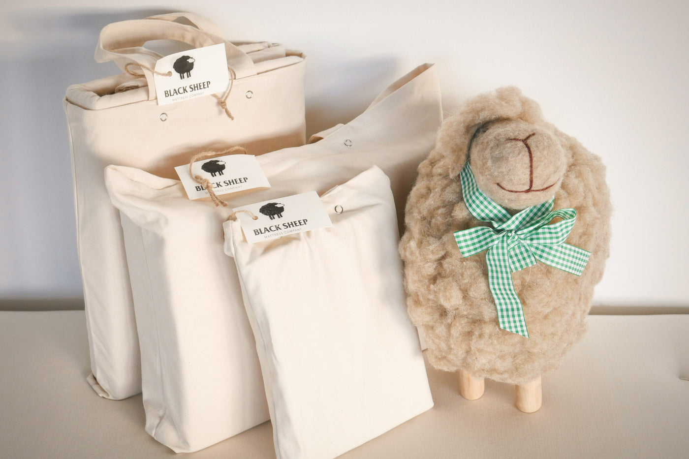 Organic cotton crib sheets in organic cotton tote bags with sheep toy next to them